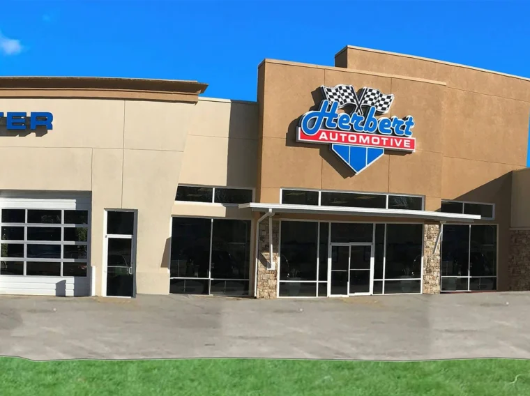 Exterior view of an automotive service center with multiple garage bays, a sign reading "Herbert Automotive" on the building, and clear primary navigation for customers arriving onsite.