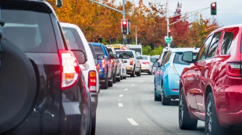 Cars stopped at a red traffic light on a multi-lane road with trees showing autumn foliage in the background, perhaps some drivers thinking about upcoming cylinder replacement or clutch replacement needs.