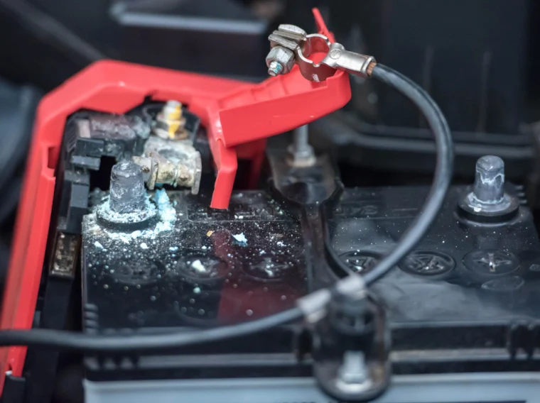 Close-up of a car battery terminal with visible corrosion and a red plastic cover partially open, highlighting the need for Battery Maintenance and timely Battery Replacement.