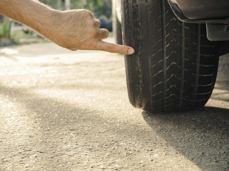 A hand points to a car tire with worn and uneven tread, suggesting the need for Tire Replacement or other Tire Services.